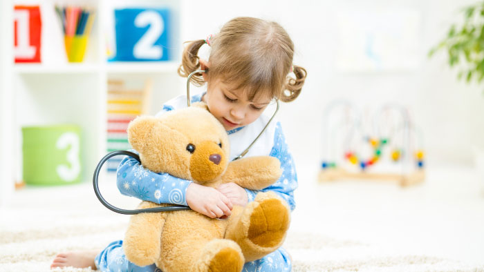 Little girl in pigtails holding stethoscope to teddy bear