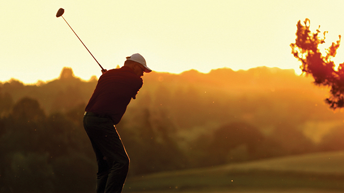 Man swinging a golf club on a golf course at dusk