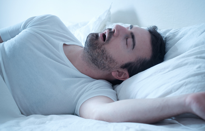 Middle aged man sleeping in bed with mouth open laying on his back