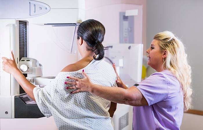 Female clinician assists women while getting a mammogram