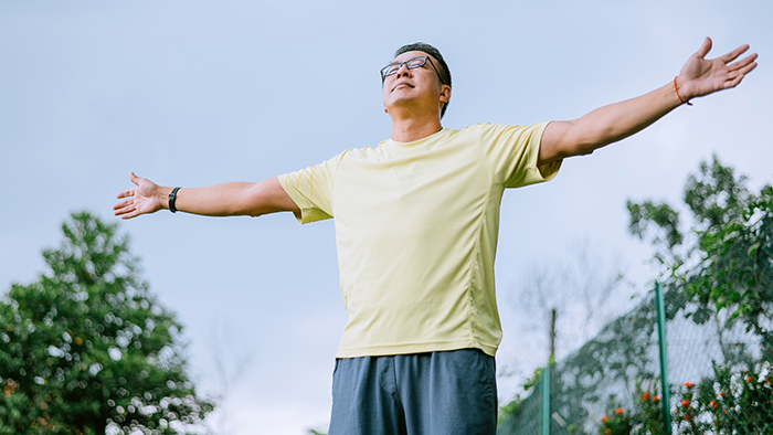 Man in yellow shirt taking a deep breath outdoors