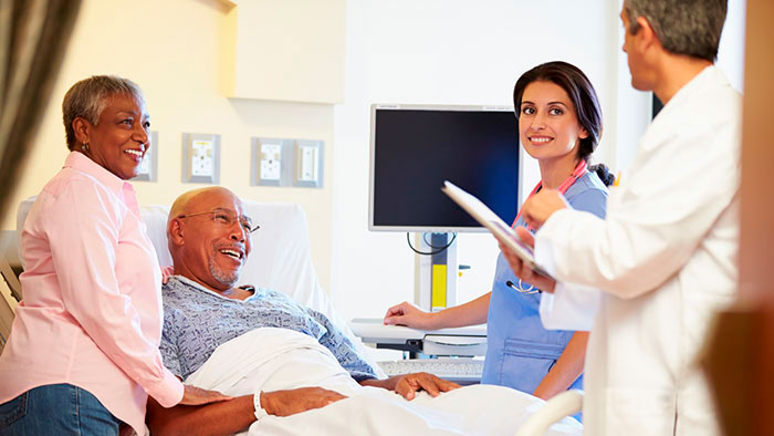 A patient is in bed with a loved one, nurse and doctor