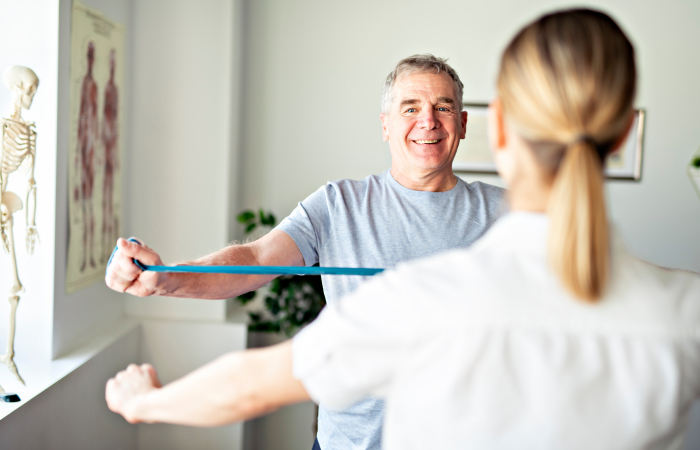 female therapist helping middle aged man with physical therapy arm stretching