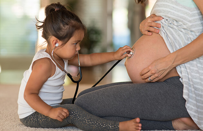 young girl putting stethoscope on her mom's bare pregnant belly