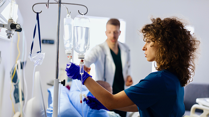 Nurse in blue adjusting an IV with doctor in background