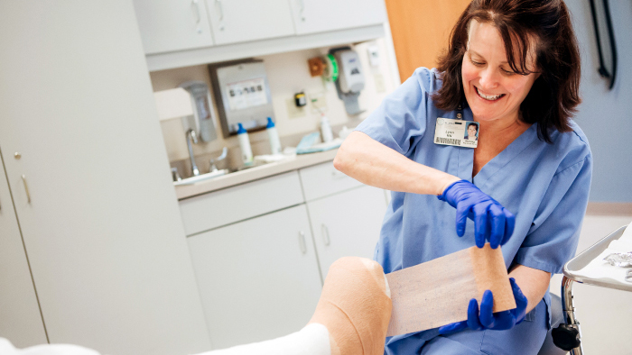 Female nurse in blue wrapping a foot wound