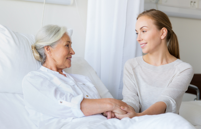 A patient is in bed with a loved one holding their hands