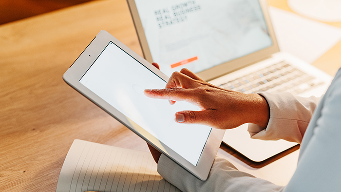 Woman tapping on tablet screen with laptop in background