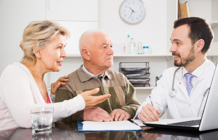 Older couple sits at table with male doctor taking notes