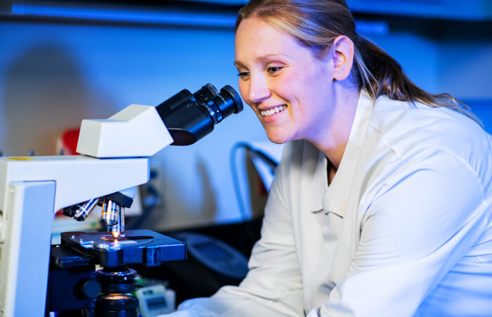 Female lab technician smiling while using microscope