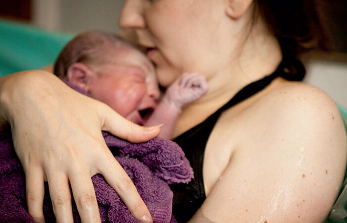 A mother hugs her new born baby wrapped in a towel
