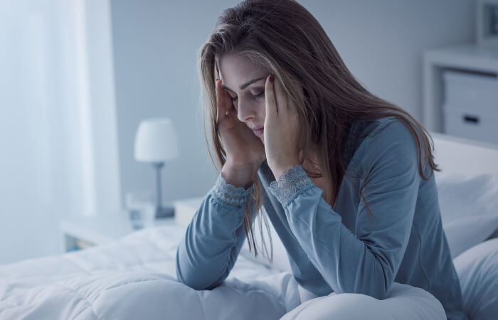 white woman rubbing her temples while laying in bed