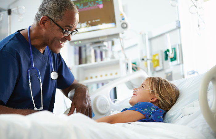 older black doctor talking to young girl laying in hospital bed both smiling