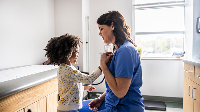 Young African-American girl and health care provider using stethoscope.