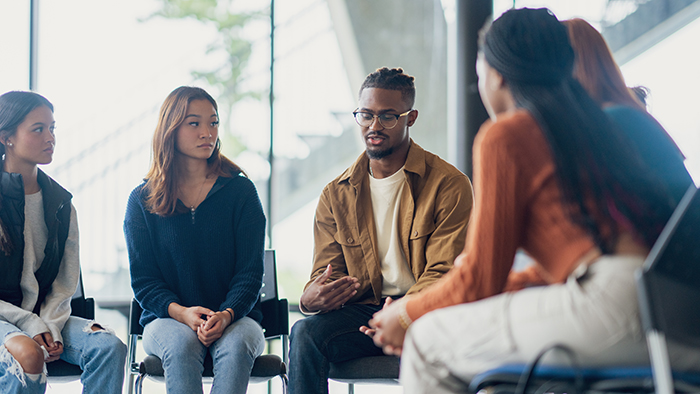group of people sitting in chairs in a circle listening to one person speak