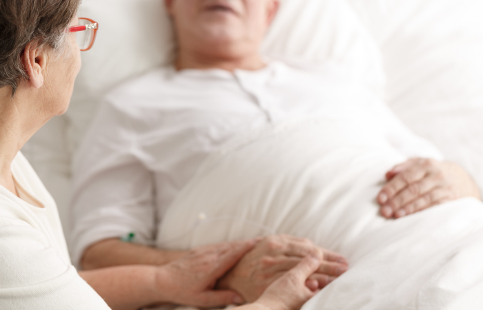 Patient in hospital bed and member of our spiritual care team hold hands