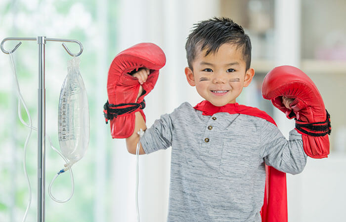 young asian boy wearing a superhero cape and boxing gloves looking at camera smiling