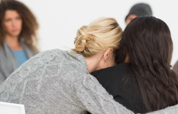 A blonde women in gray consoles a women in black during a support group