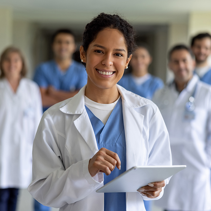 A female doctor stand with a tablet in a hallway while other providers stand in the background