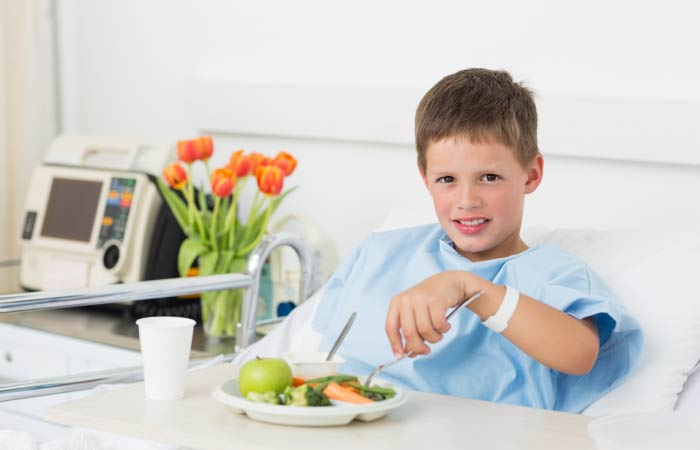 young boy eating food in hospital bed