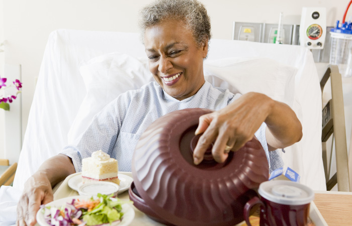Female patient in hospital room smiling and looking at her colorful meal
