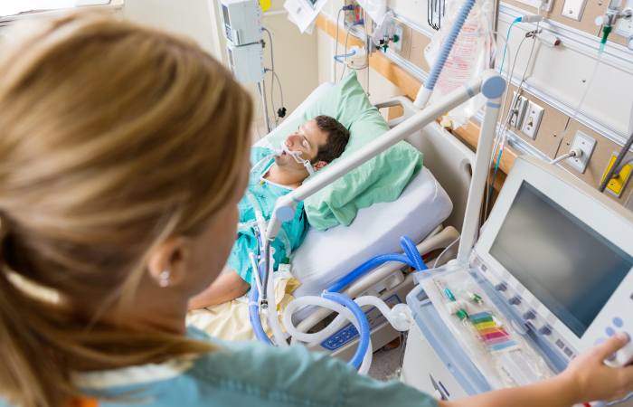Nurse monitors intubated patient laying in bed