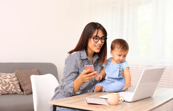 Mother holding baby while searching for information on laptop and phone