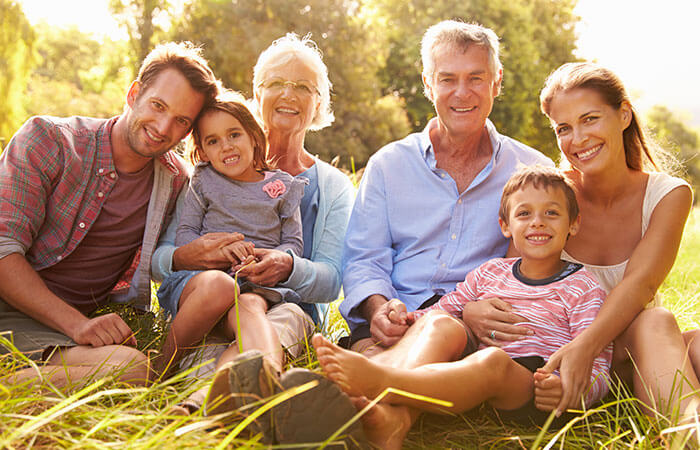 6 person family sitting outdoors in the grass including grandma and grandpa, mom and dad, and two daughters