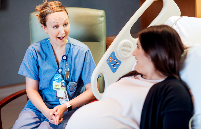 Woman looking surprised while talking to pregnant woman laying in hospital bed