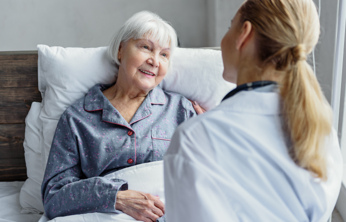 Young female doctor talking to elderly patient in hospital setting