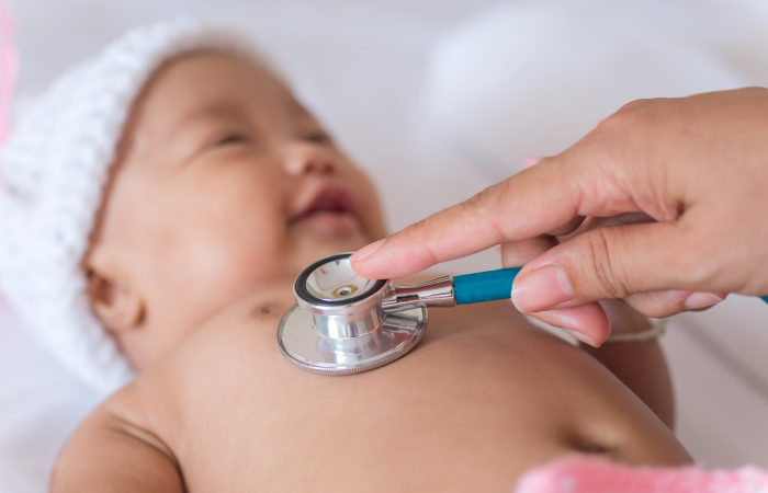 newborn baby wearing white hat with a stethoscope on their chest