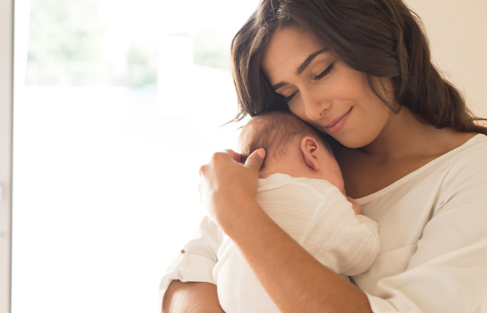 A mother in white holds her infant against her chest