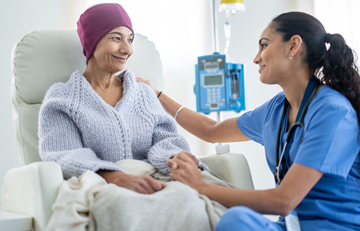 Female nurse sitting with female cancer patient while she receives treatment