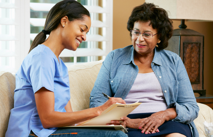 Young black nurse taking notes while mature black woman talks both are sitting on a couch