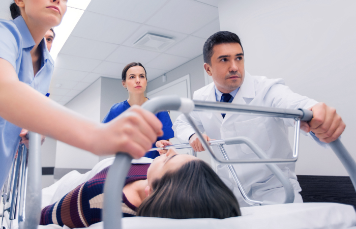 a male doctor and two female doctors pushing a gurnee with a patient on it towards the emergency room