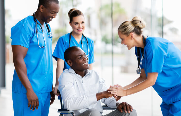 three physicians in scrubs greeting man in wheelchair to the hospital