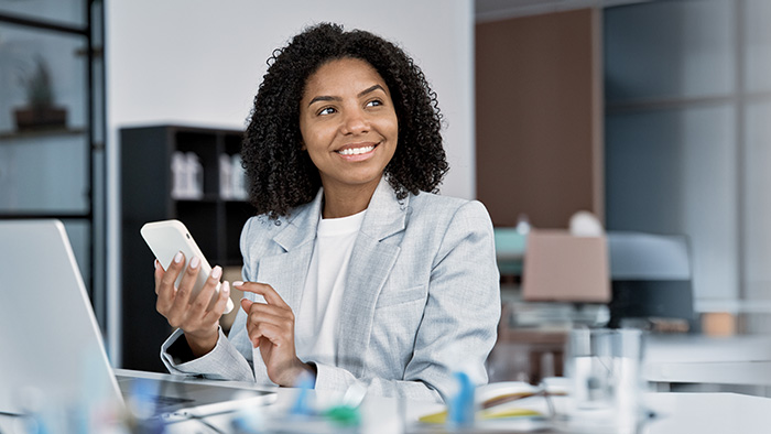Young woman at computer with cell phone gazing out
