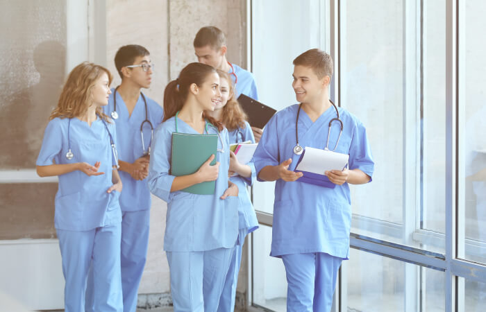 Younger medical students talk and walk down a hallway in front of a window