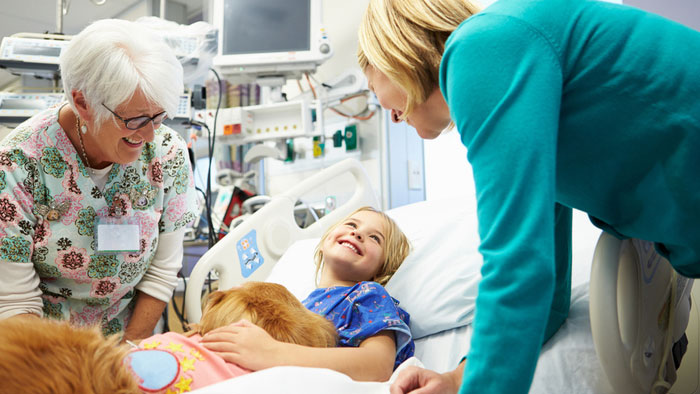 Mom and senior woman volunteering talks with young girl patient in hospital bed