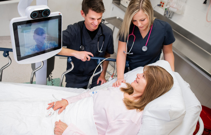 two physicians in person and one remote physician helping patient in hospital bed